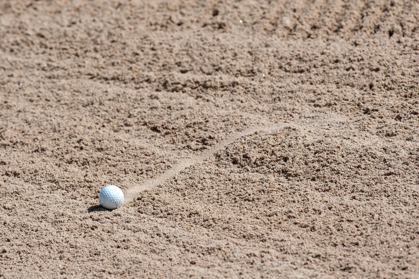 Golfball im Sandbunker mit Schlagspur